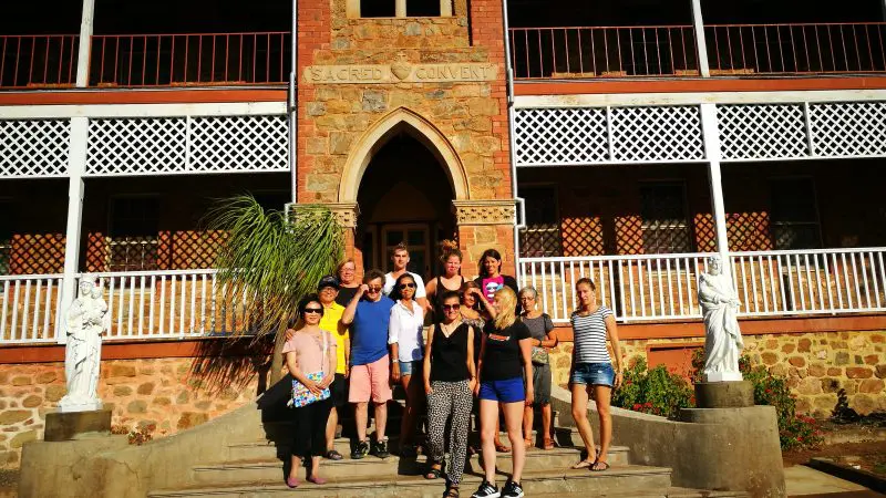 Tour group from the 8-Day Perth to Exmouth Return Tour smiles on steps of Sacred Convent, a heritage-listed stone landmark in WA.