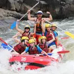 Thrill-seekers in helmets and life jackets smile on a Barron River rafting adventure, setting off from Port Douglas, ready for excitement.