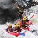 Adventure seekers in helmets and life jackets navigate thrilling Barron River rapids on a half-day white-water rafting near Cairns.