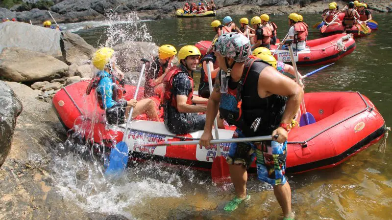 Adventure-seekers in helmets white-water raft Barron River with expert guide; thrilling rafting tours depart from Port Douglas.