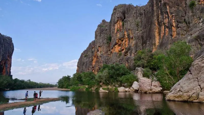 a cliff face beside a river with people on one side