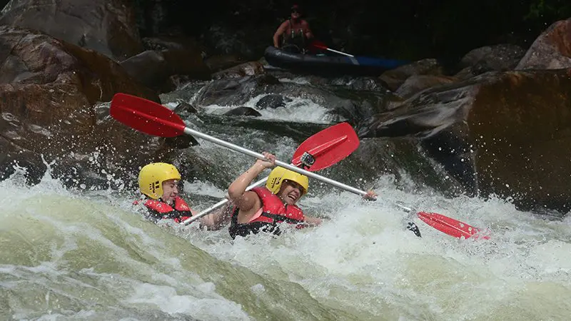 Two adventurers in helmets paddle a kayak through thrilling white-water rapids on a full-day Mission Beach rafting experience.