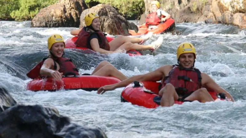 Four adventurers experience Half Day River Tubing with Foaming Fury, floating on red tubes down a scenic rocky river amid lush greenery.