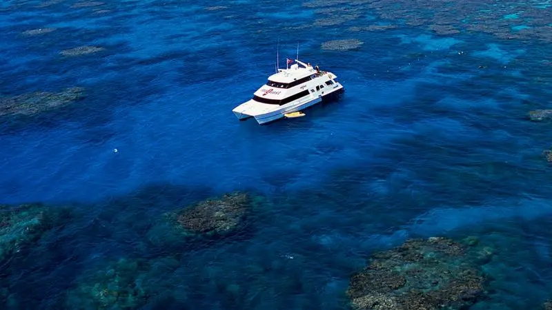 Aquaquest Outer Reef Dive: White boat on crystal-clear blue water above colourful coral reefs in a tropical paradise ocean setting.