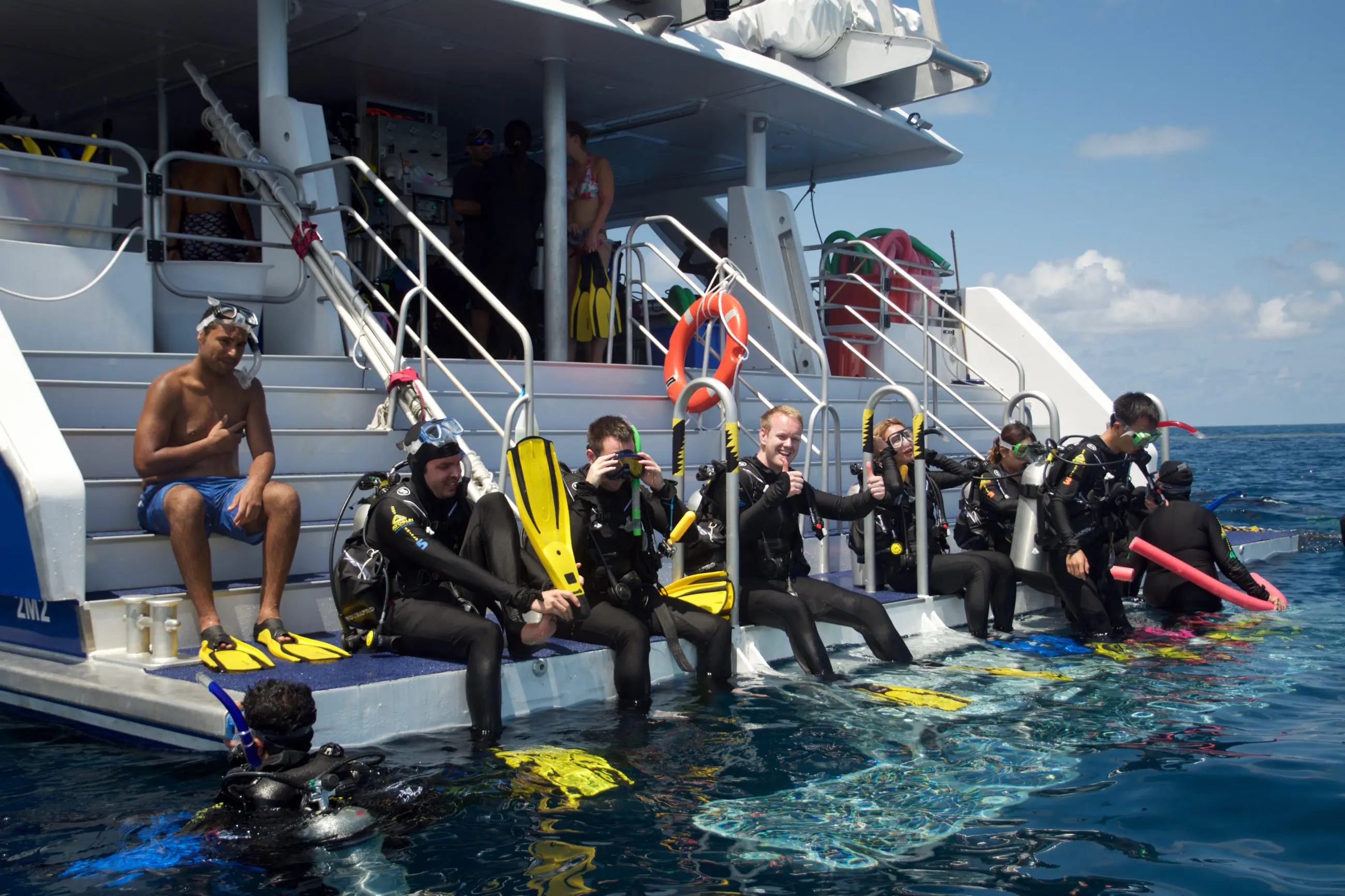 Scuba divers in PADI Open Water Course 2 sit on a boat’s edge, fully equipped with fins and kit, preparing to dive into the sea.