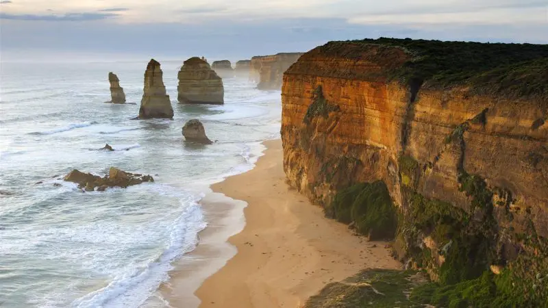 Majestic limestone stacks stand along a golden sandy beach on the Great Ocean Road’s 1 Day 12 Apostles Tour with Go West Tours.