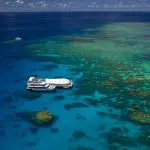 Tour boat anchored by the Great Barrier Reef Activity Platform in pristine turquoise waters beneath a vibrant, sunny sky.