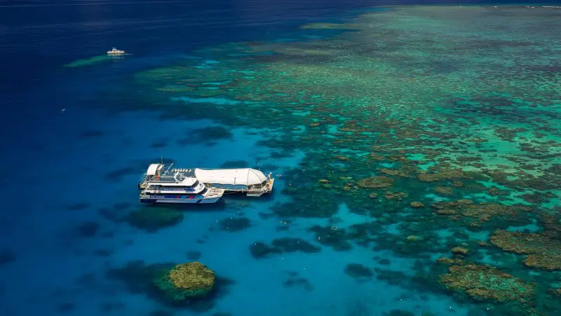 Tour boat anchored by the Great Barrier Reef Activity Platform in pristine turquoise waters beneath a vibrant, sunny sky.