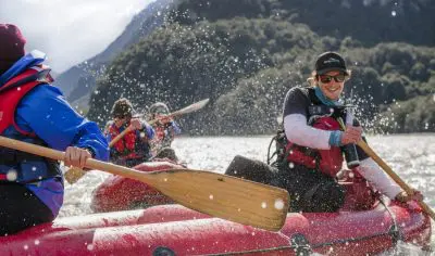 Adventurers in life jackets paddle red Funyaks on the scenic Dart River with splashing water and majestic mountains in the background.