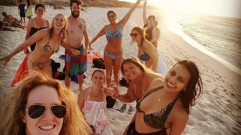 Friends on the 6 Day Perth to Exmouth Tour take a sunset beach selfie in swimsuits, capturing Australia’s stunning coastline.