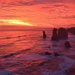 Spectacular red and orange sunset over Great Ocean Road cliffs, waves crashing below—unforgettable scenic tour on Australia’s coastline.