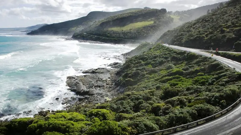 Experience the stunning Great Ocean Road: a scenic coastal drive with ocean views, lush green hills, and Go West’s 1 day guided tour.