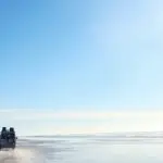 4WD vehicle drives along sandy beach during a 3 Day K'gari Adventure, with dormitory accommodation near Rainbow Beach beneath clear blue skies.