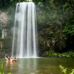 Three travellers raise arms in a vibrant green pool, enjoying a Fully Guided Ultimate East Coast Melbourne to Cairns adventure tour.