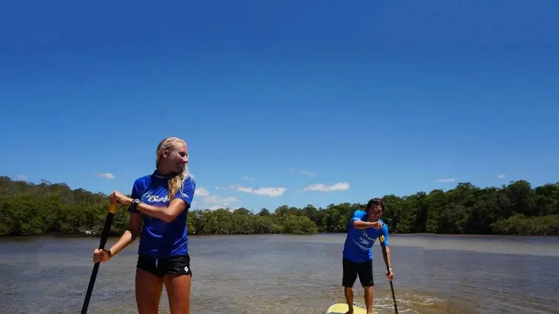 Two people paddleboarding on tranquil waters during the Byron Bay Group 2 five-hour stand up paddle board tour experience.
