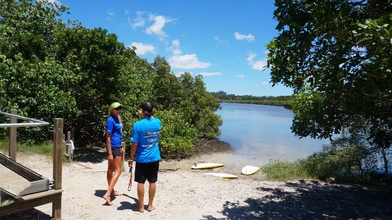 Experience a Private Byron Bay 2 Hour Stand Up Paddle Board Nature Tour with two people in blue shirts beside paddleboards.