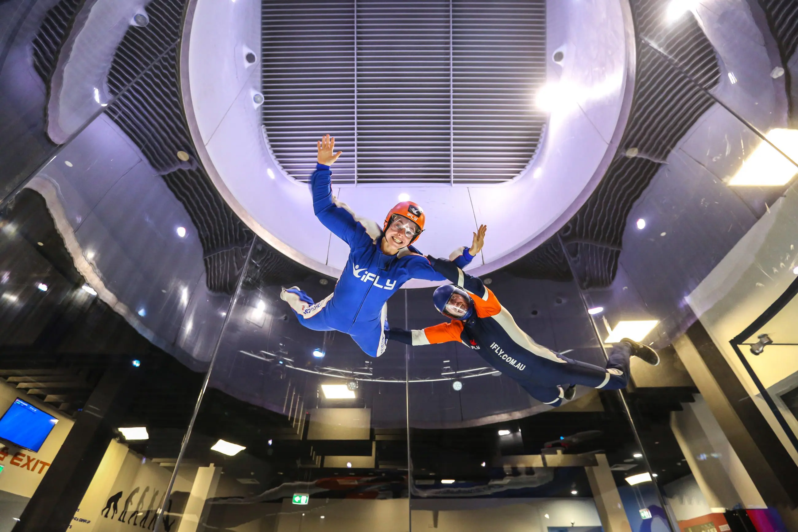 Two people experience indoor skydiving at iFLY Family and Friends, smiling in flight suits and helmets inside a state-of-the-art wind tunnel.