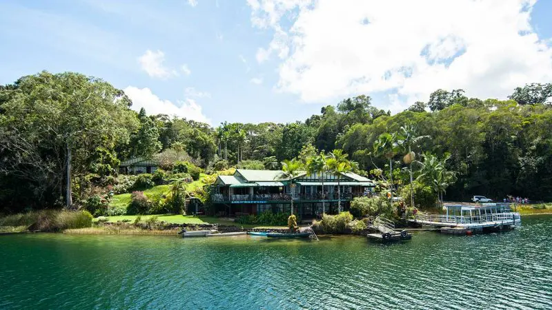 Scenic lakeside house amid lush trees with a jetty, evoking a Northern Experience similar to Paronella Park Entry in Queensland.