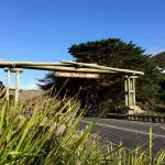 Iconic wooden archway entrance to the 1 Day Great Ocean Road 12 Apostles Tour by Go West Tours, surrounded by lush greenery and blue sky.