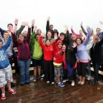 Tour group on wooden decking by Phillip Island beach smiles and waves during Penguin Parade Tour, enjoying scenic sea views.