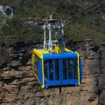 Experience breathtaking views as a blue and yellow cable car soars above a rugged gorge on the ultimate 1 Day Blue Mountains Tour.