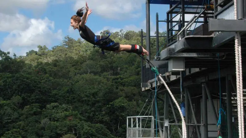 Thrill-seeker leaps from Australia’s Only Bungee Skypark, soaring above lush green forest under a vibrant blue sky, ultimate adventure.