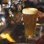 Close-up of a hand holding a frothy pint of beer at a bar after the 1 Day Noosa Everglades Explorer with Everglades Eco Safaris.