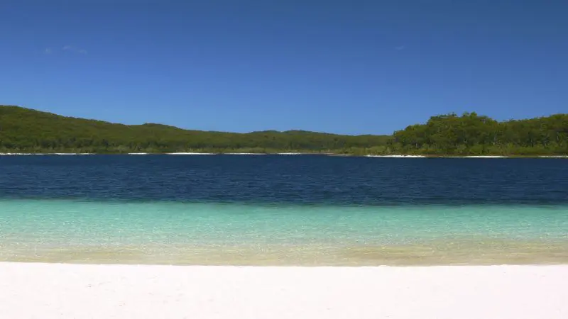Stunning white sand beach on the 2 Day K’gari Fraser Island Tag Along Adventure, with crystal clear blue waters and lush green hills.