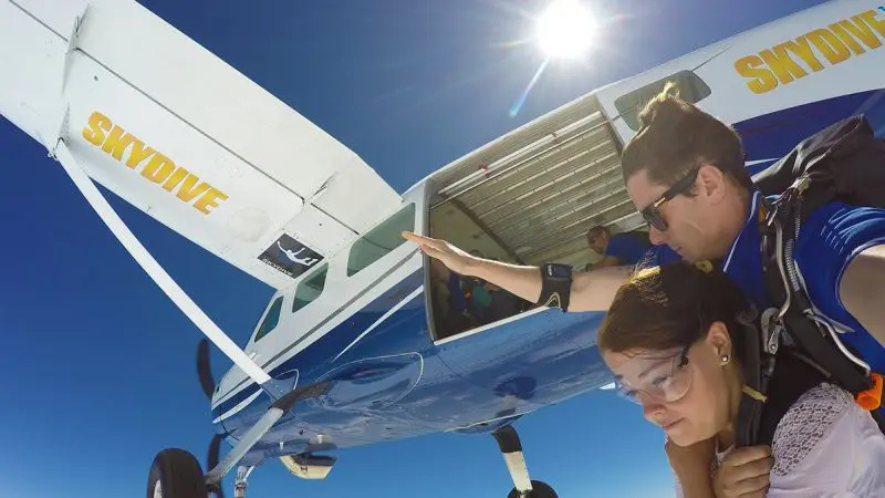 Experience the thrill of a Skydive Sydney tandem jump as two people leap from an aeroplane, surrounded by sunlit skies and scenic clouds.
