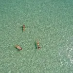 Three people relax floating on crystal-clear turquoise waters during a Remote 1 Day K'gari Fraser Island tour experience in Australia.