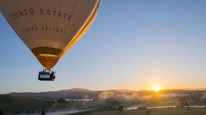 Experience a breathtaking sunrise hot air balloon flight over Melbourne with Global Ballooning Australia, soaring above misty valleys.