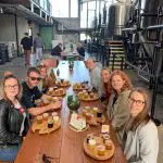 Smiling group tasting craft beer flights at a vibrant brewery during an Arvo Session Behind The Barrel Half Day Tour, posing for photo.