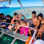 Tourists aboard a glass-bottomed boat admire vibrant coral reefs near a docked ship during a one-day Outer Reef Fitzroy Island tour.
