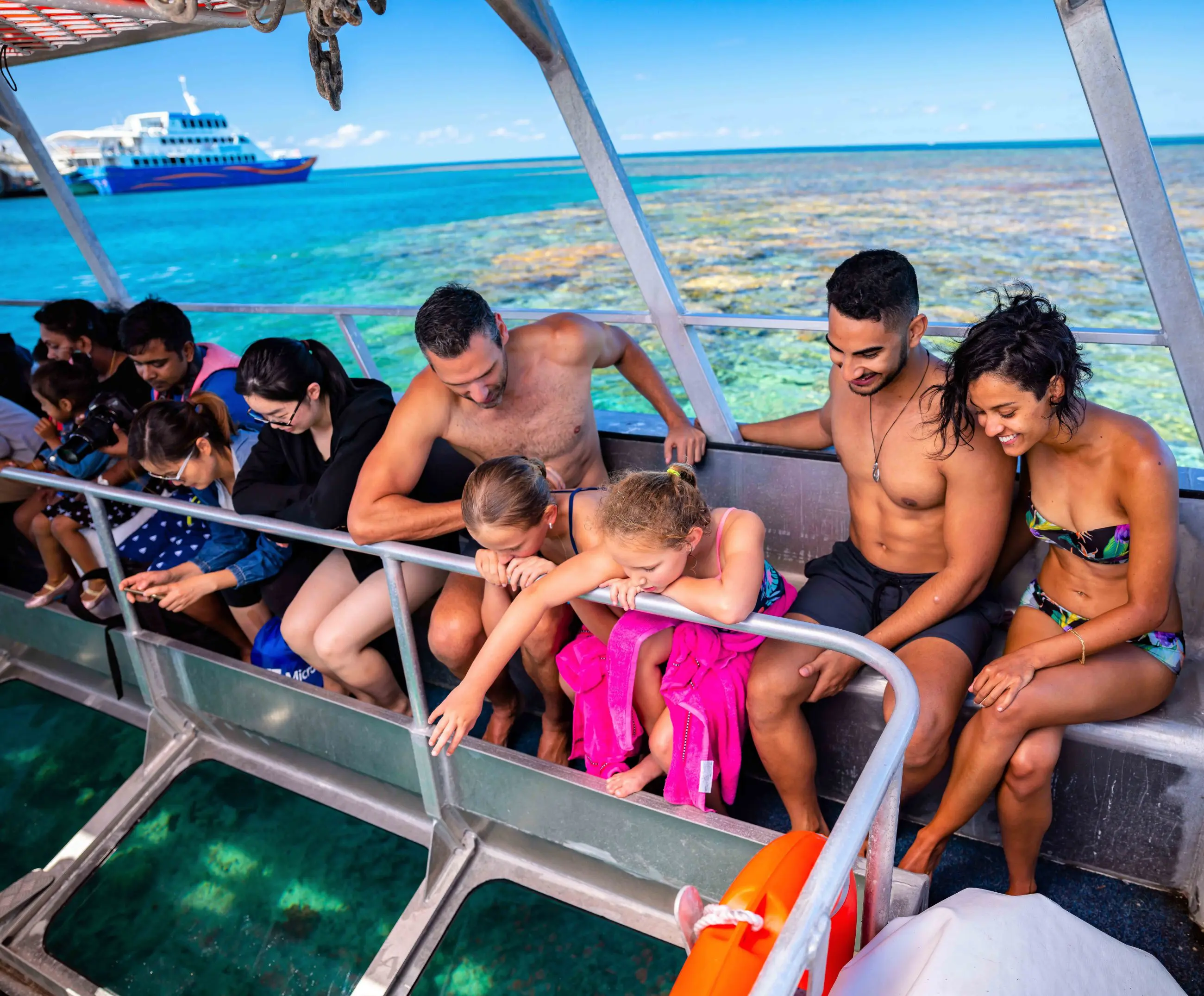 Tourists aboard a glass-bottomed boat admire vibrant coral reefs near a docked ship during a one-day Outer Reef Fitzroy Island tour.