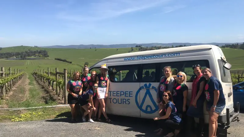 Women smiling by a branded Teepee Tours van during a relaxed Yarra Valley Winery Tour in sunlit vineyards, perfect for group outings.