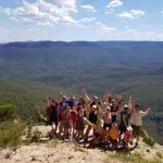 Smiling group celebrates on a rocky Blue Mountains lookout after a scenic waterfall walk and social lunch during guided day tour.