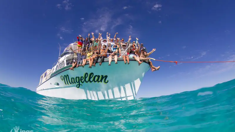 Guests enthusiastically wave from the Magellan boat on crystal-clear blue water during a Full Day Whale Shark and Humpback Interaction Tour.