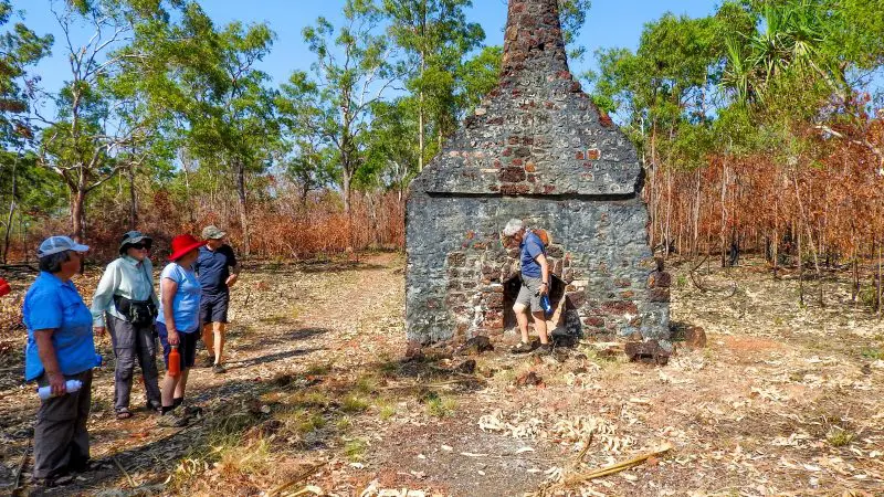 Tour group explores ancient stone chimney ruins in Kakadu Arnhem Land, surrounded by dry woodland under a bright, clear blue sky.