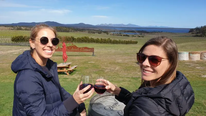 Stylish women in sunglasses clink red wine glasses at a scenic vineyard during a Wineglass Bay Full Day Tour via Richmond.