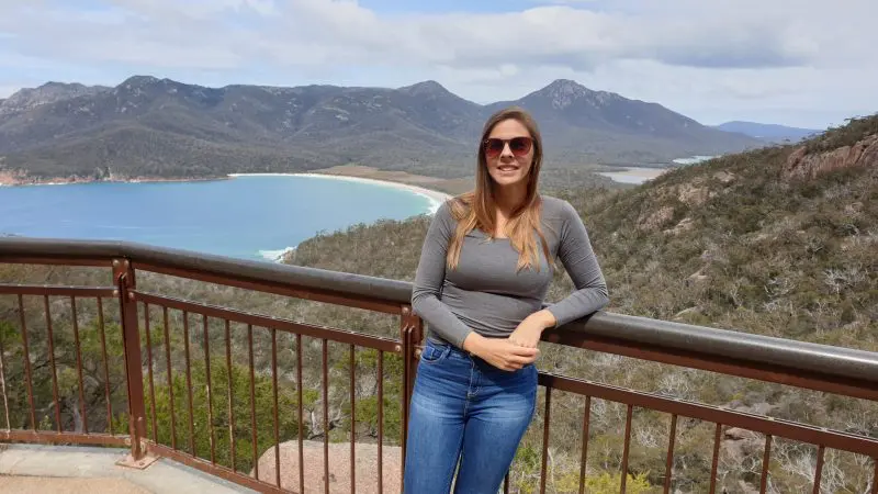 Stylish woman in sunglasses stands by a railing, overlooking the breathtaking Wineglass Bay Full Day Tour via Richmond landscape.