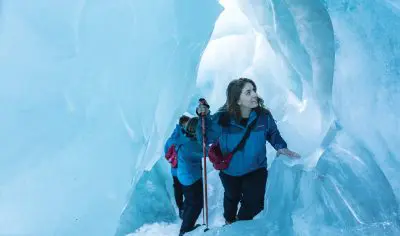Adventurers in winter gear journey through a narrow icy cave on a Franz Josef Glacier tour, encased by vivid blue glacier walls.
