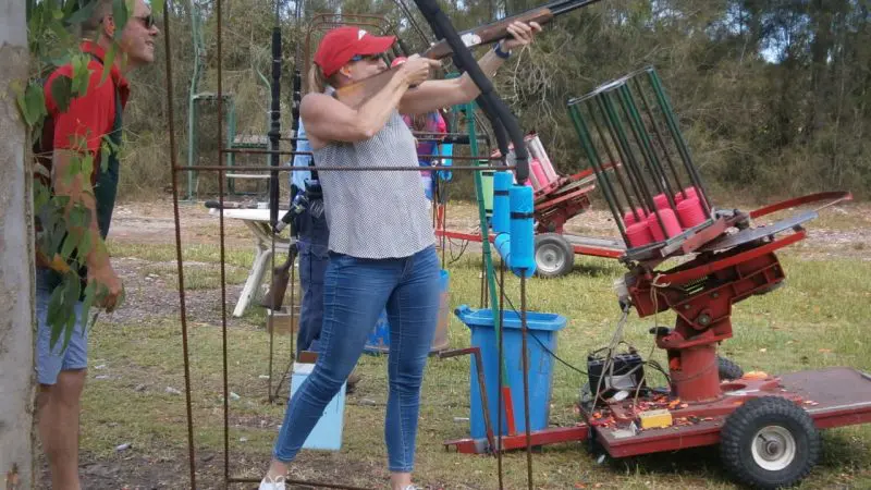 A woman takes part in Have A Go Clay Target Shooting at a range, guided by a man; visible clay targets and equipment enhance the scene.