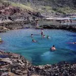 Adventurers swim in a stunning seafront rock pool on a 3 Day K’gari tour with dormitory accommodation at vibrant Rainbow Beach.