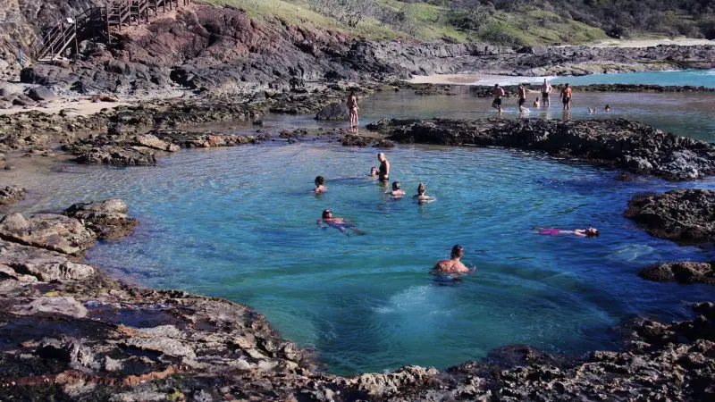 Adventurers swim in a stunning seafront rock pool on a 3 Day K’gari tour with dormitory accommodation at vibrant Rainbow Beach.