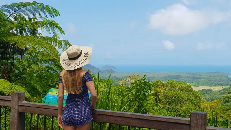Explore the breathtaking views of Cape Tribulation as a woman in a sunhat enjoys Daintree’s lush rainforest and crystal blue sea.