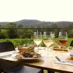 Elegant outdoor dining table set with gourmet dishes and four wine glasses, boasting panoramic Yarra Valley views and rolling hills.