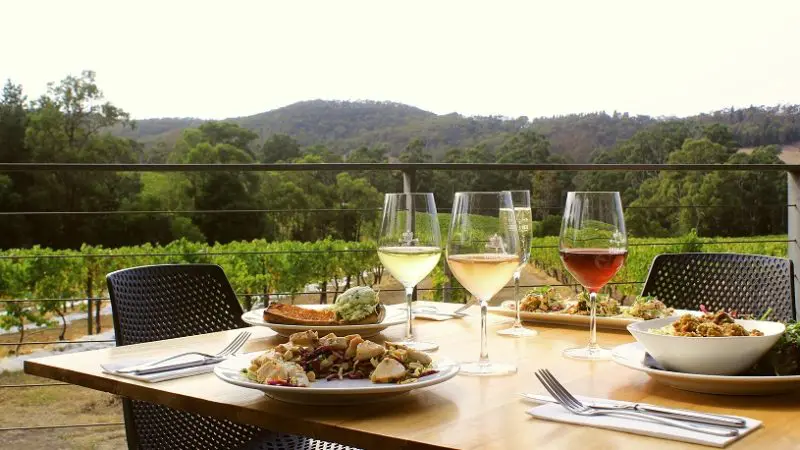 Elegant outdoor dining table set with gourmet dishes and four wine glasses, boasting panoramic Yarra Valley views and rolling hills.