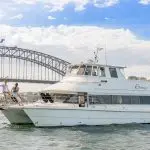 Luxury white yacht gliding on Sydney Harbour, two guests at the bow enjoying canapés during an exclusive Vivid Lights cruise experience.
