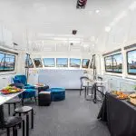Luxurious Sydney Harbour Vivid Lights Cruise interior with gourmet canapés, plush blue seating, and breath-taking city vistas through panoramic windows.