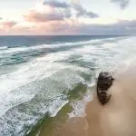 Iconic rusted shipwreck on Fraser Island’s sandy shore at sunset, highlighted during the Fraser Experience Tour beneath dramatic clouds.